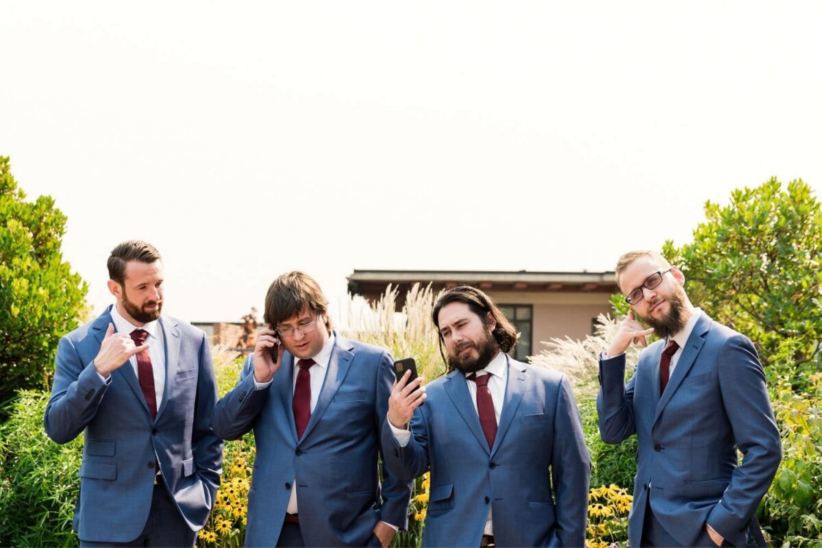 A funny photo of a groom and his groomsmen wearing wedding attire and all checking their phone with funny faces