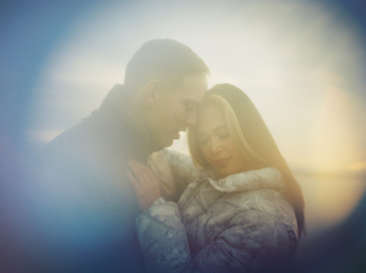 A cinematic portrait taken with film in Victoria BC. A couple is cuddling and there are blurred reflections. 