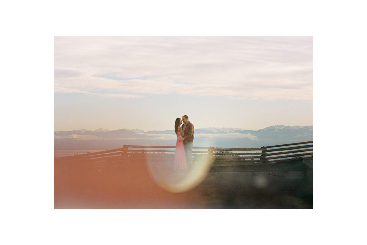 A creative engagement portrait taken on film at Macaulay Point Park in Victoria BC. The couple is kissing and the Olympic mountains are in view behind them. 
