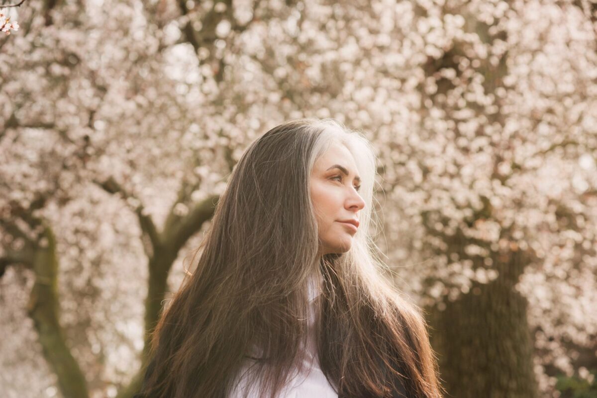 Beauty portrait with a woman over 50 with grey and black hair. The portraits were taken at Thunderbird Park in Victoria BC during the spring when the cherry blossoms were blooming. This was a combination of a fashion shoot and a glamour or artistic shoot, with bespoke customized art portraits.