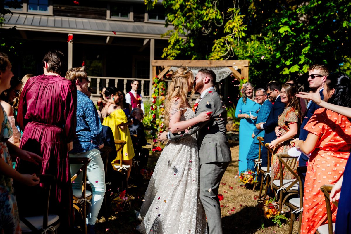 Bride and groom kissing while people toss rose petals
