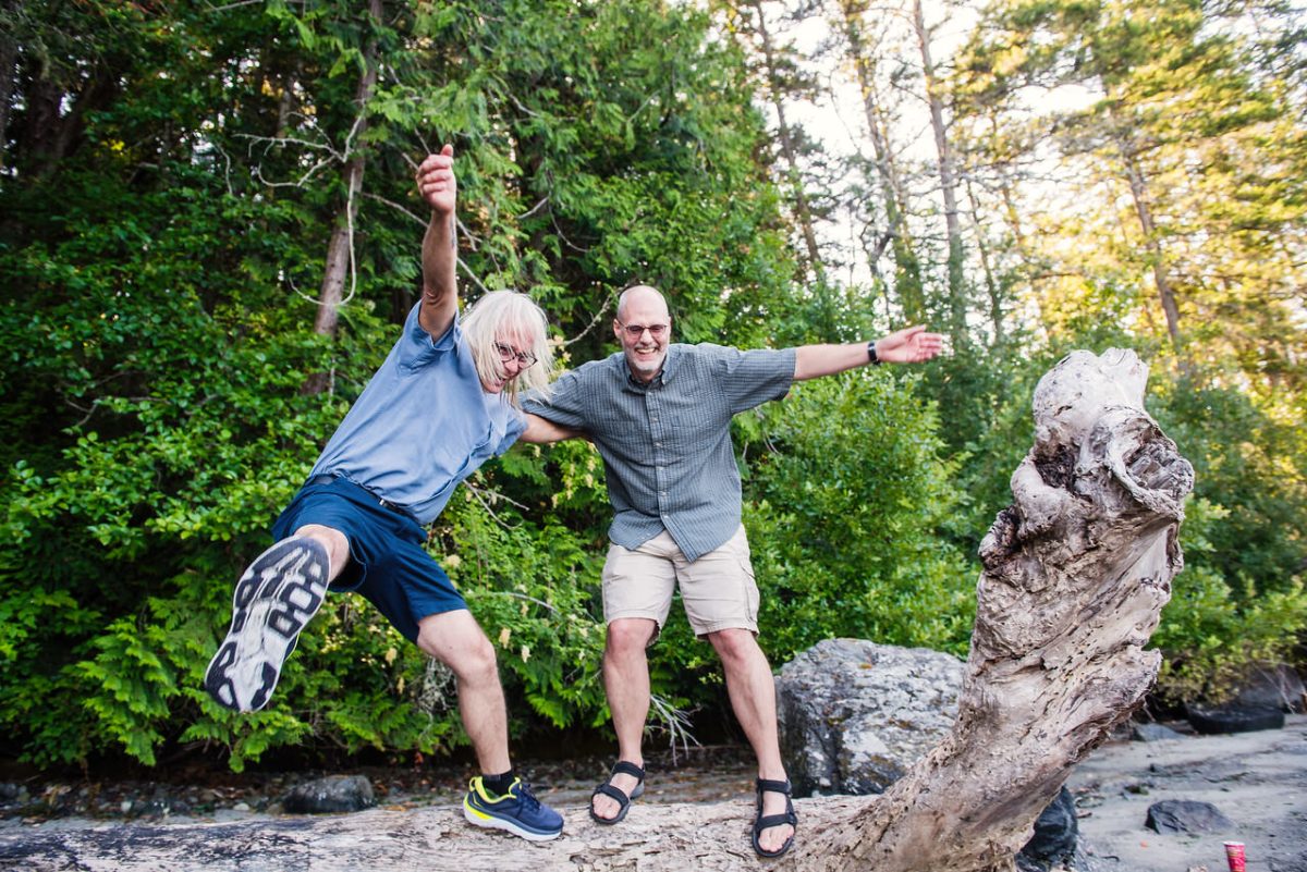 Adult brothers jumping off a log in East Sooke Park on a deserted beach during a family portrait session.