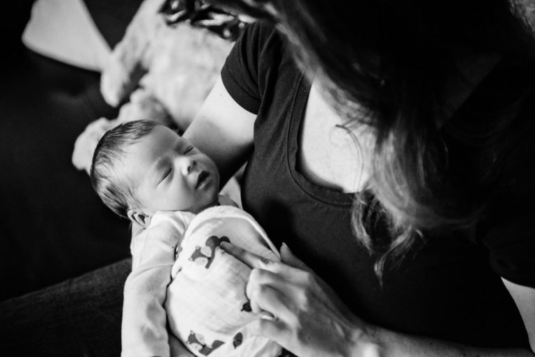 A mother holds her newborn baby. Photo is taken in black and white and it's a documentary family portrait.