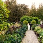 A bride and groom walks along the fall gardens in front of Hatley Castle among some of the ruins. This is a candid photo of the couple enjoying a brief moment before the reception.