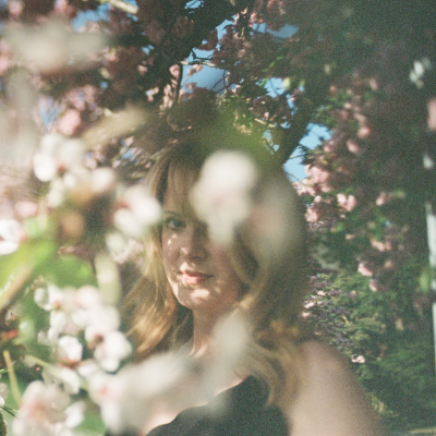 A creative film photo on analog 35mm film of a red haired woman surrounded by cherry blossoms. It is an abstract portrait to celebrate a birthday.