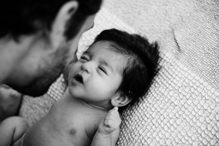A father is making faces at his baby girl. This is a natural and candid black and white newborn photograph.