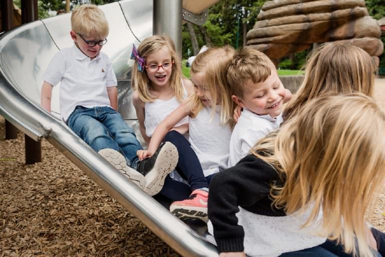 Kids piling up on a slide during a lifestyle candid family portrait session in Victoria BC at Beacon Hill Park