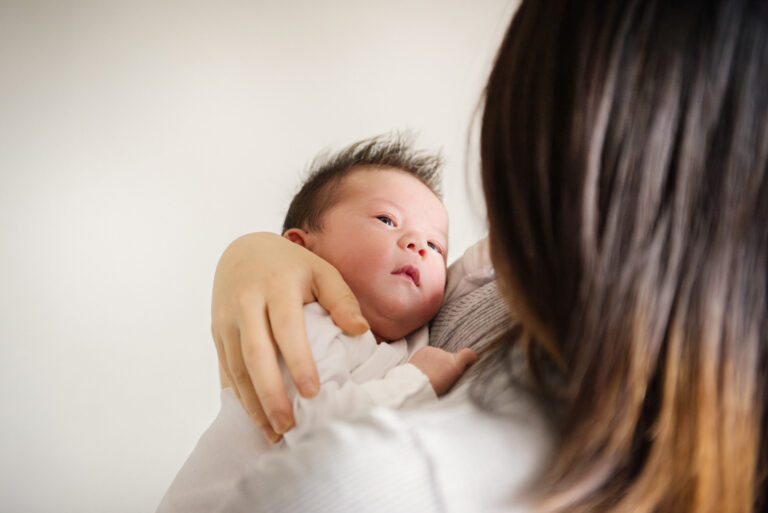 Natural candid newborn photograph in colour of a mother holding her baby in the nursery.