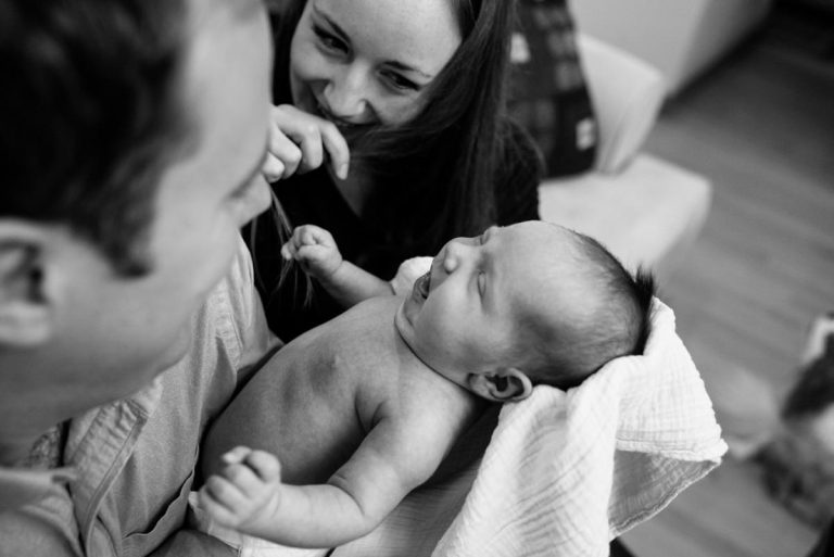 Parents hold their newborn baby girl as they giggle. The photo is in black adn white and taken in Victoria BC.