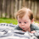 A funny baby portrait of a baby with a full head of hair cross eyed as he looks at a blanket. This is a colour photo taken in a family's backyard in Victoria BC