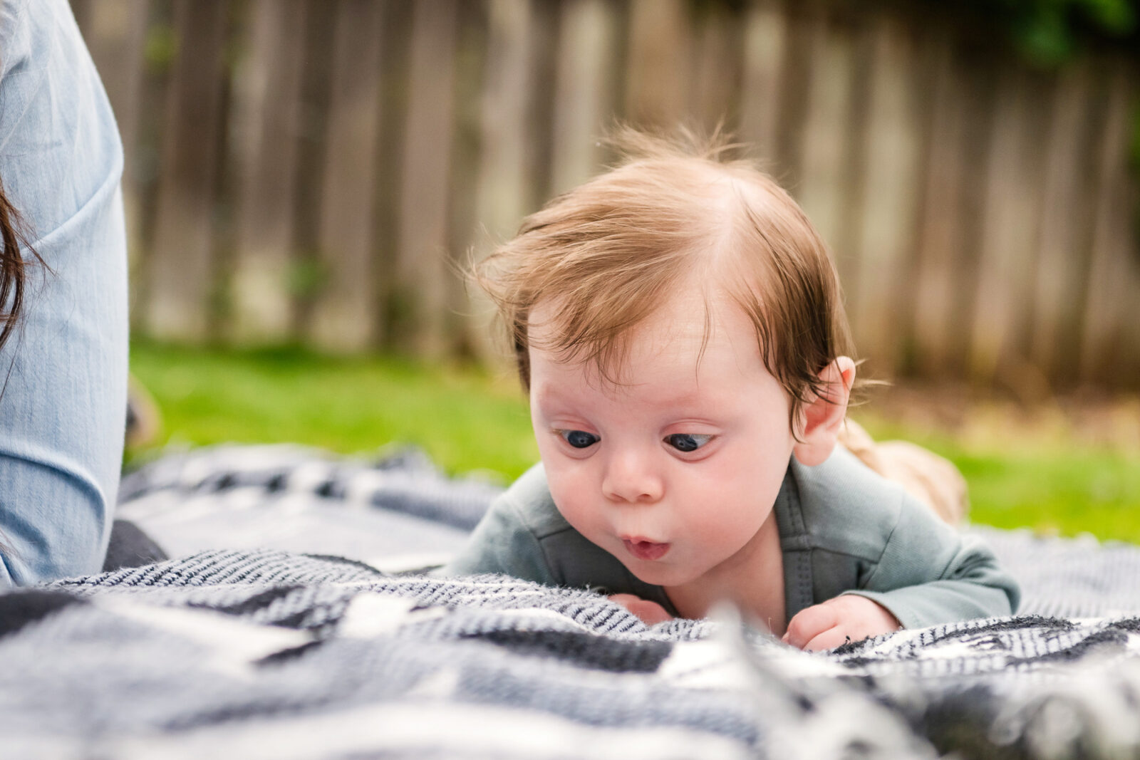 A funny baby portrait of a baby with a full head of hair cross eyed as he looks at a blanket. This is a colour photo taken in a family's backyard in Victoria BC