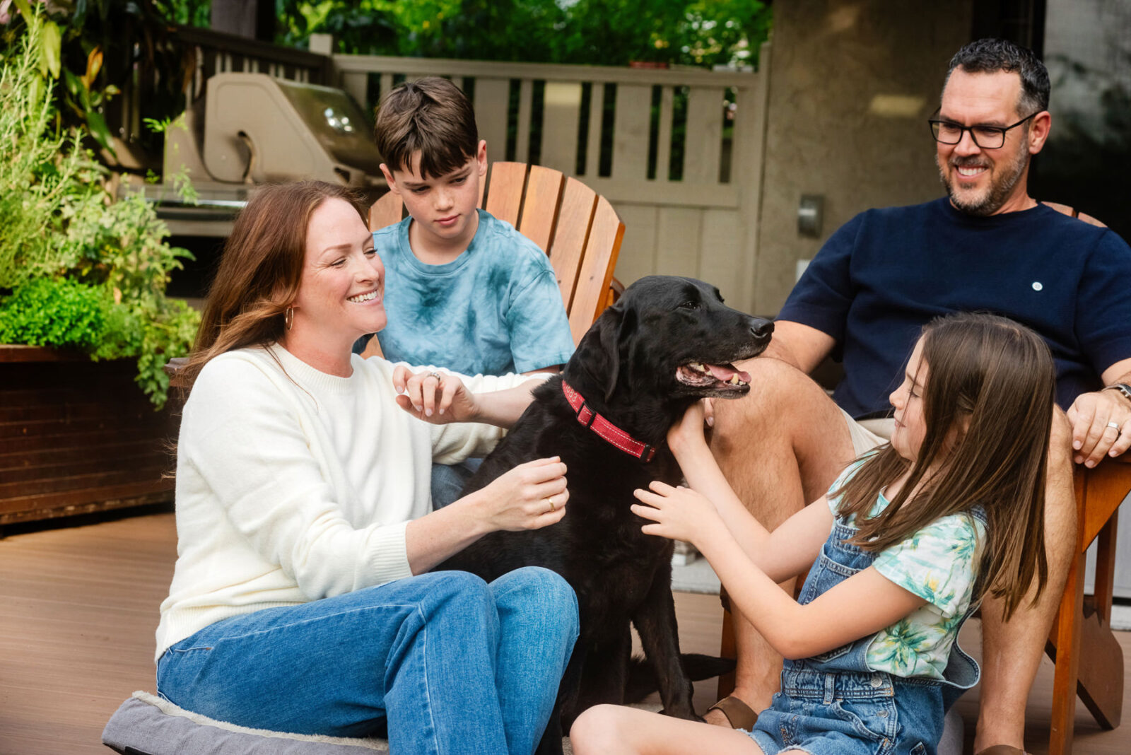 Family playing with their dog on their back patio. They are laughing and the photo is in colour.