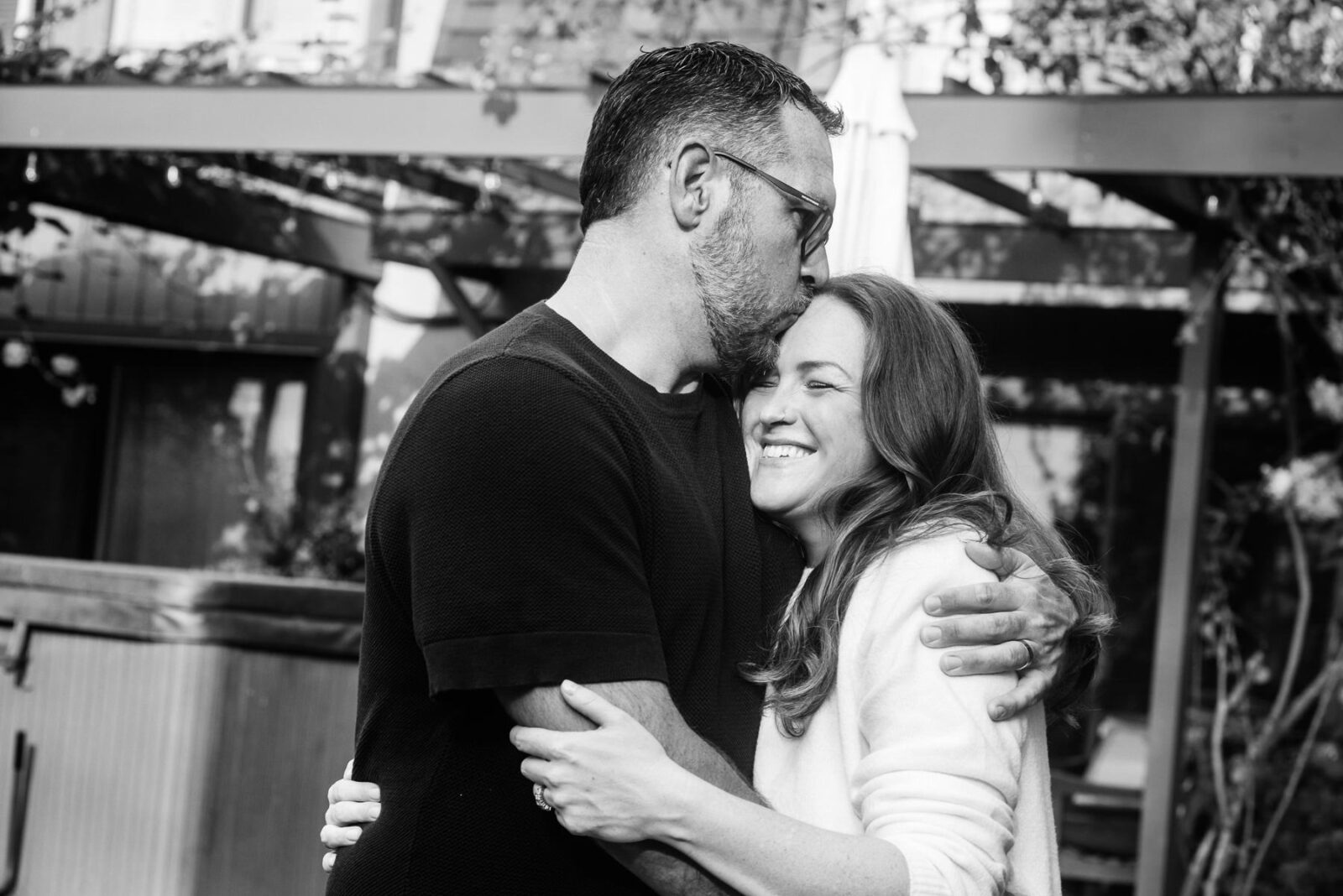 A man kisses his wife's forehead as she giggles.