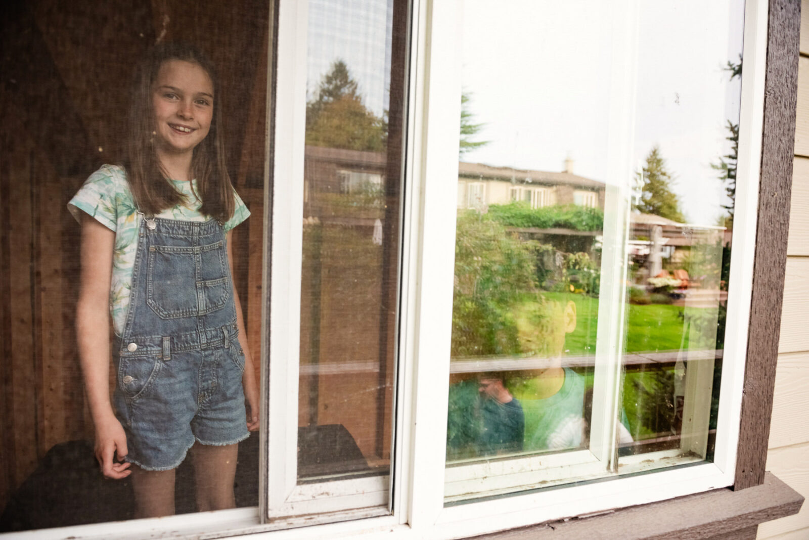 A brother and sister look out the window of their treehouse in their backyard in Victoria BC