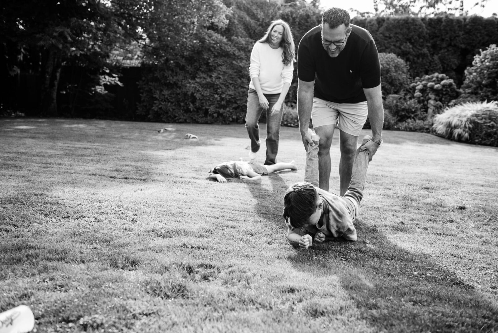 Family playing wheelbarrow game on their lawn The kids have fallen to the ground.