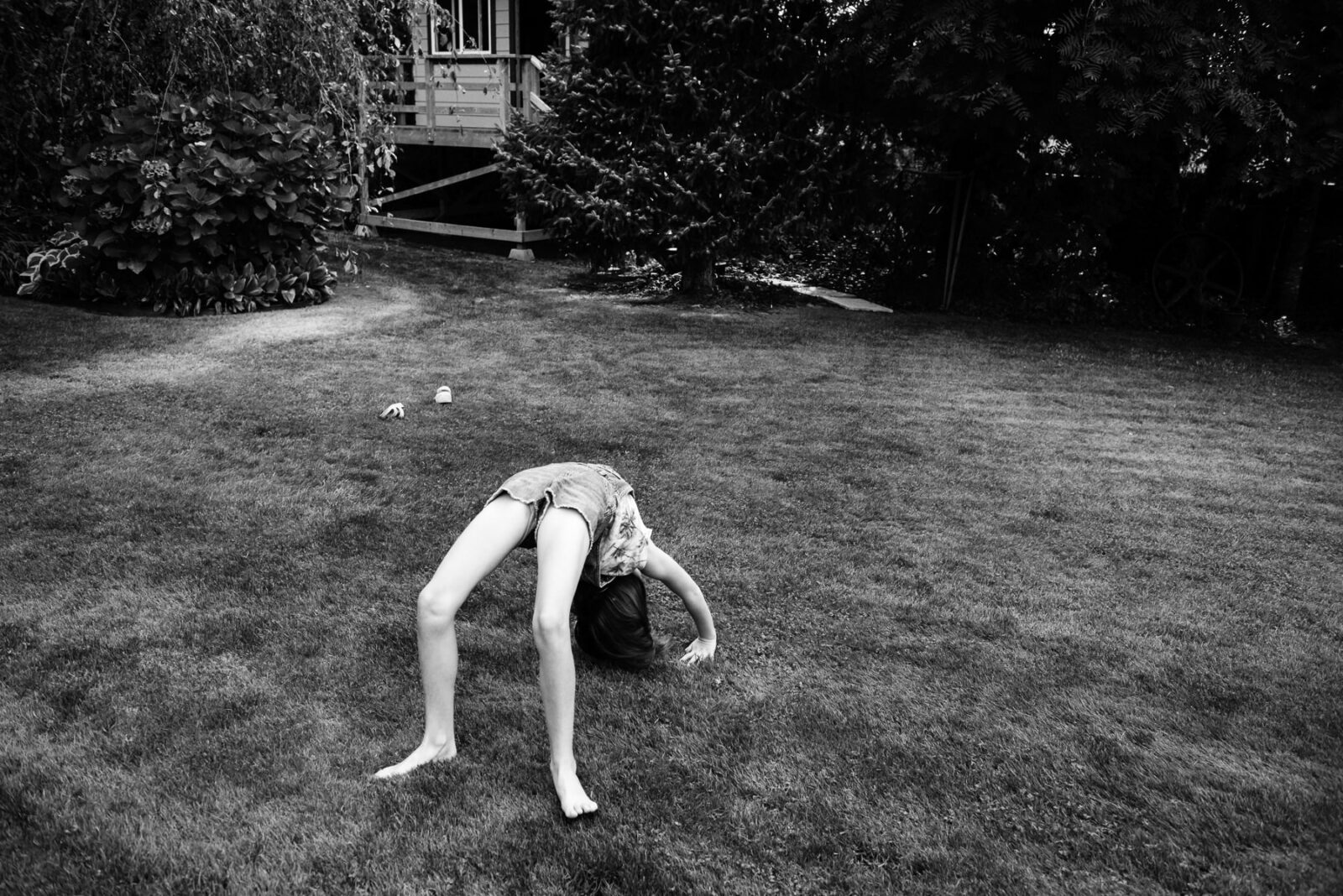 A girl does a back handstand in her backyard. This is a documentary family photo in black and white.