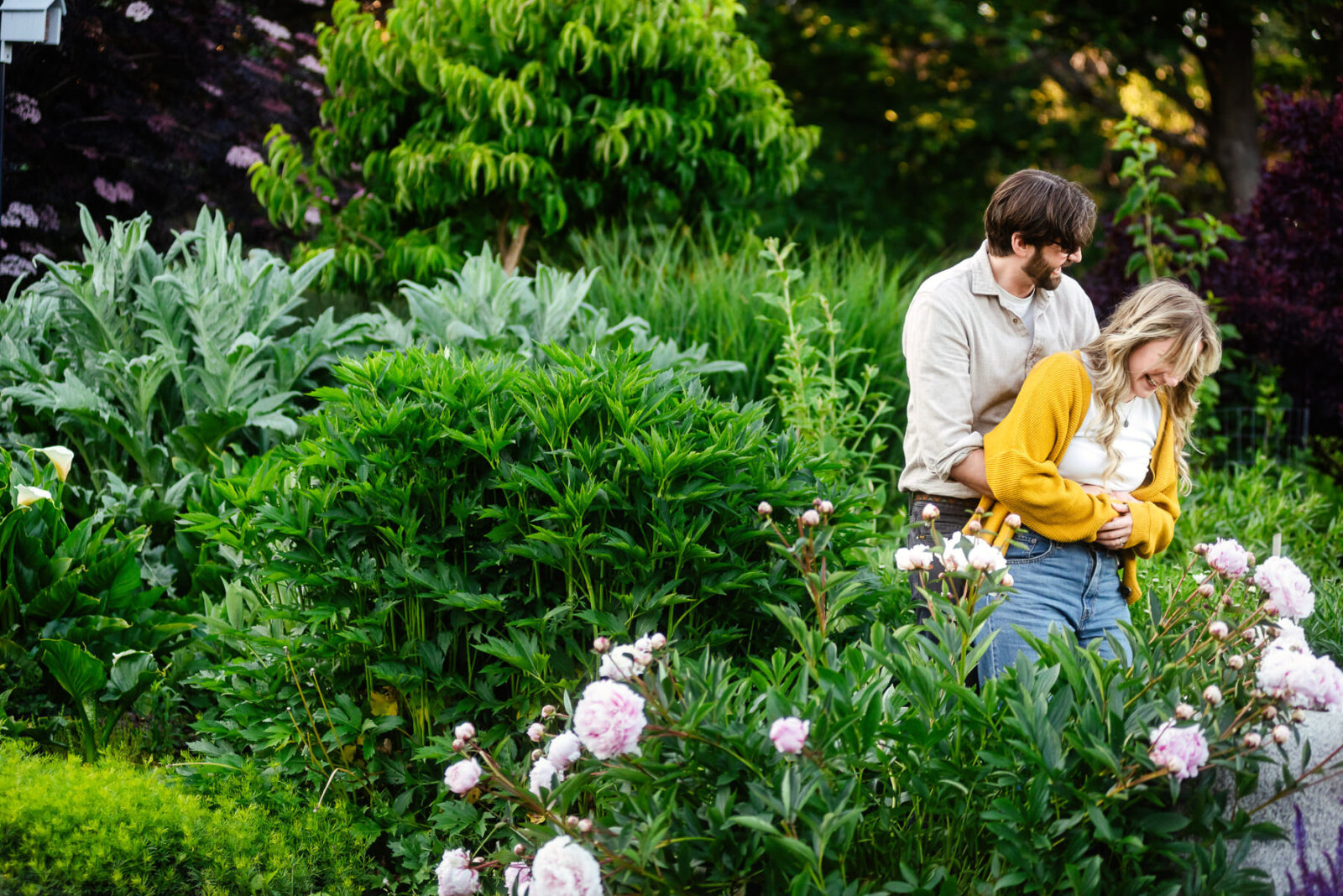 A couple laughs and looks at each other playfully during their engagement photo session in a garden in Victoria BC