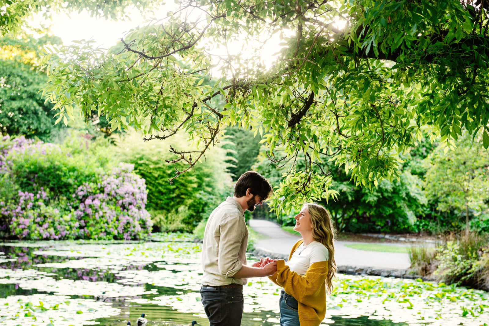 A couple stands and plays around a lily pond in Beacon Hill Park in Victoria BC at sunset.
