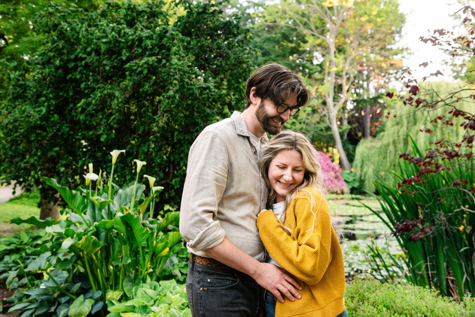 A couple snuggles in front of the tall reeds and lily pond.