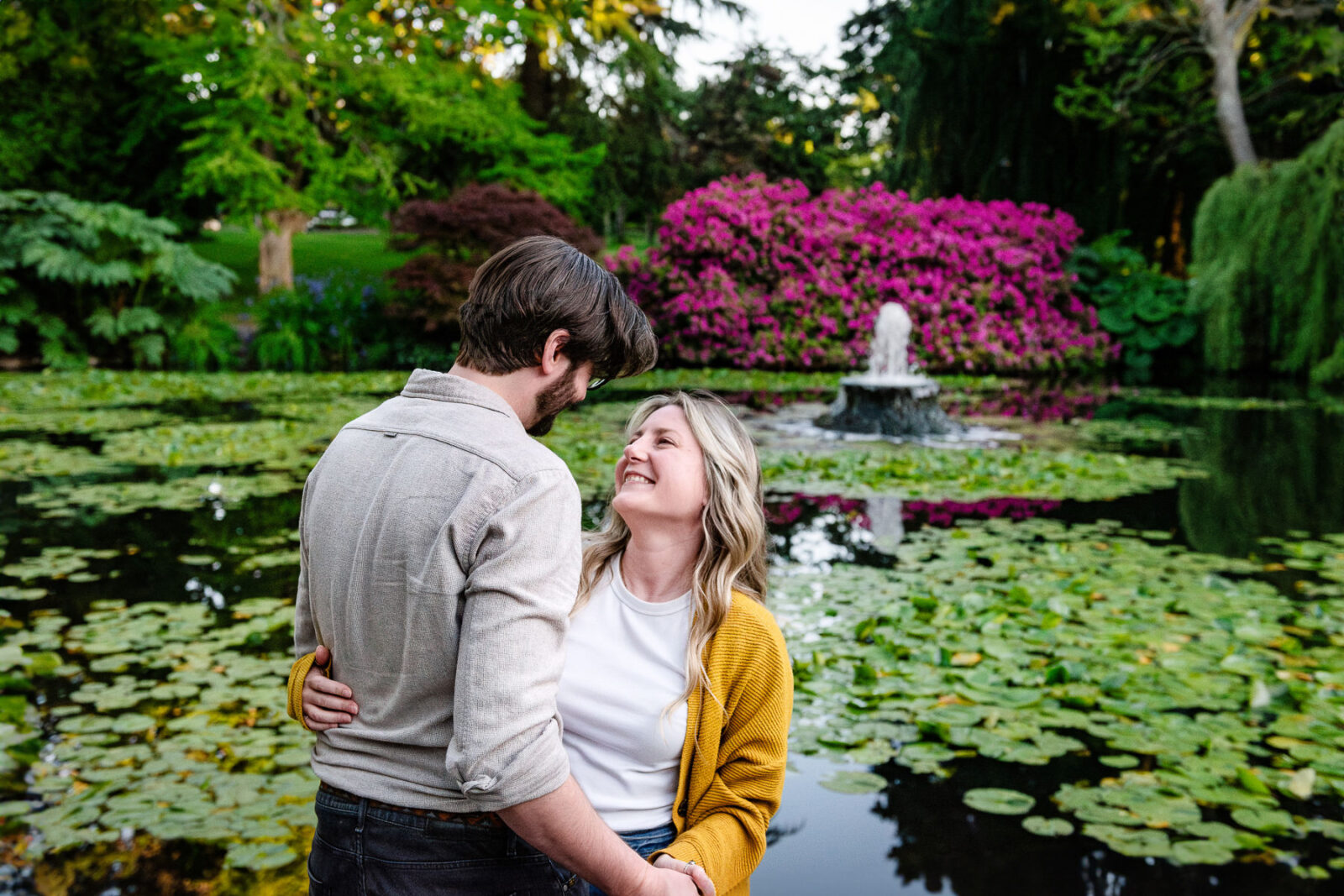 A couple looks at each other in front of the fountain in one of the Beacon Hill Park lily ponds in Victoria BC