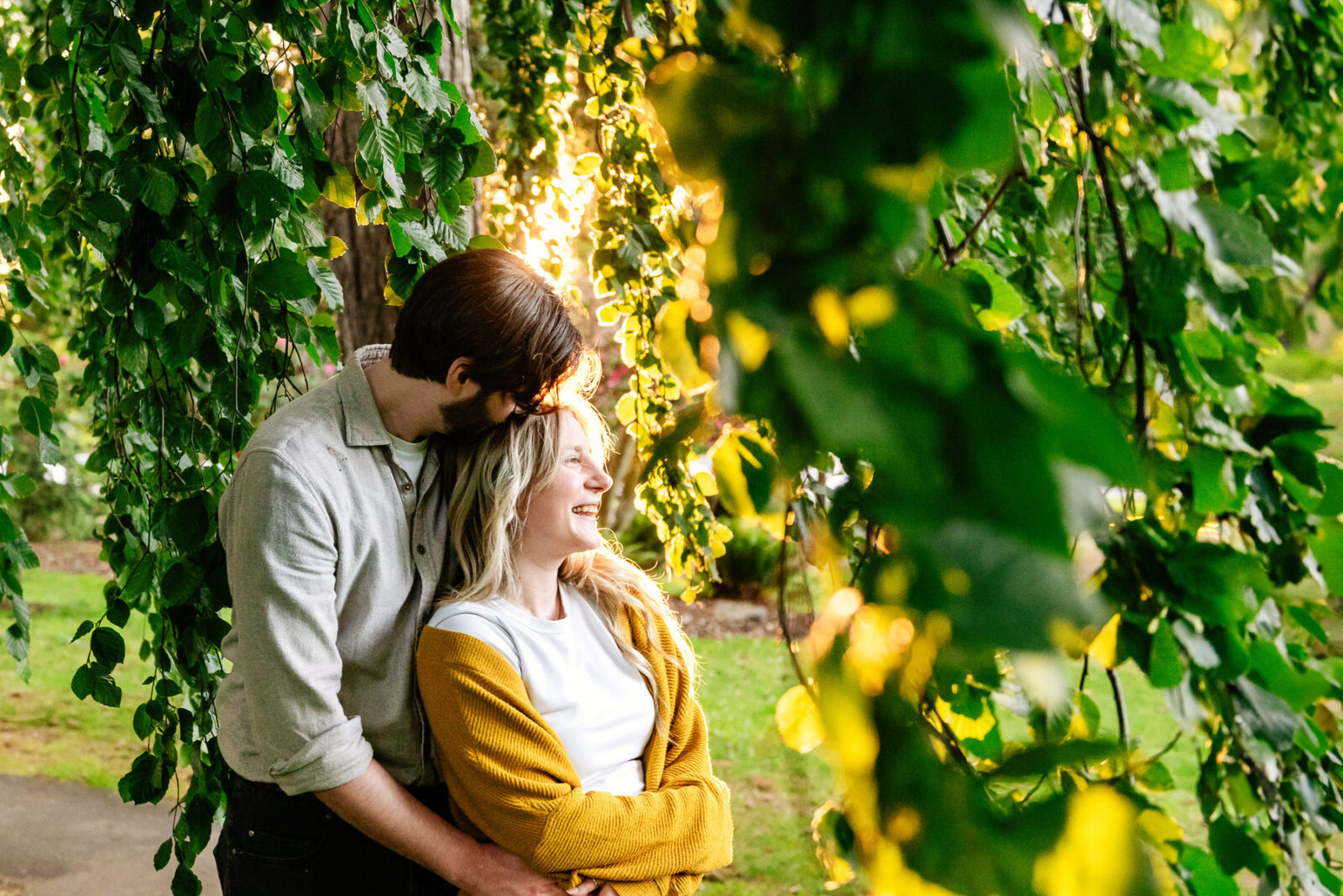 A sunset engagement portrait of a couple among the trees on the Douglas Street side of Beacon Hill Park in Victoria BC