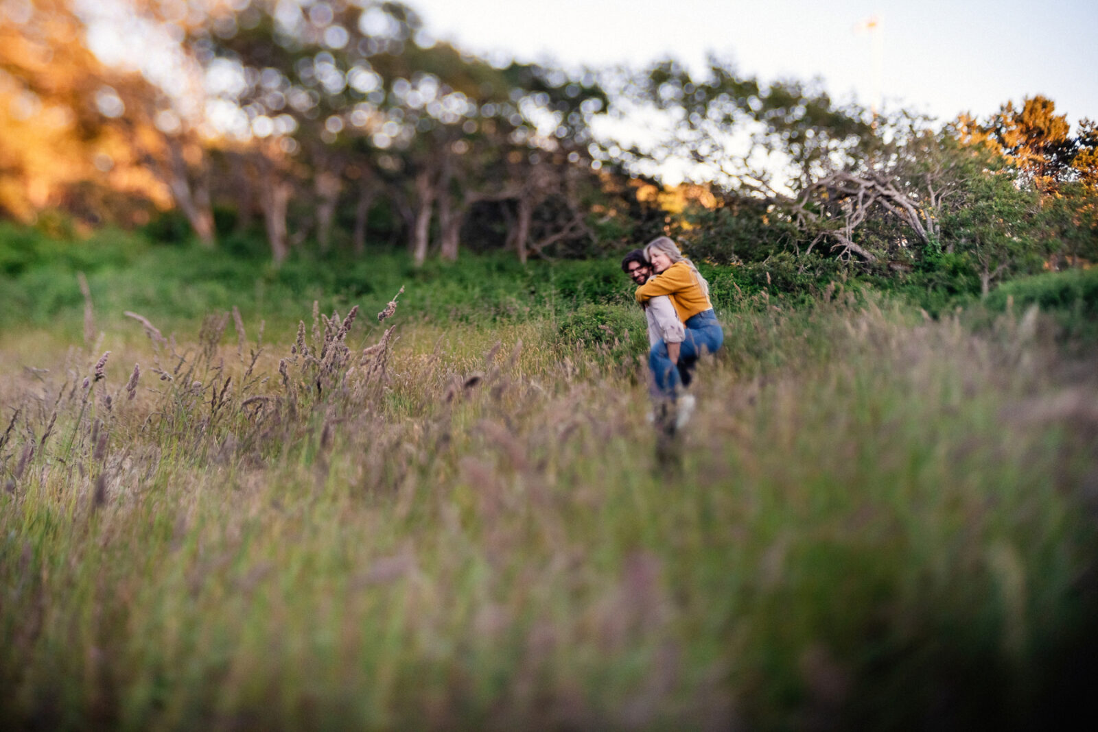 A tilt shift portrait of a couple having a piggy back ride in the field behind Beacon Hill Park in Victoria BC