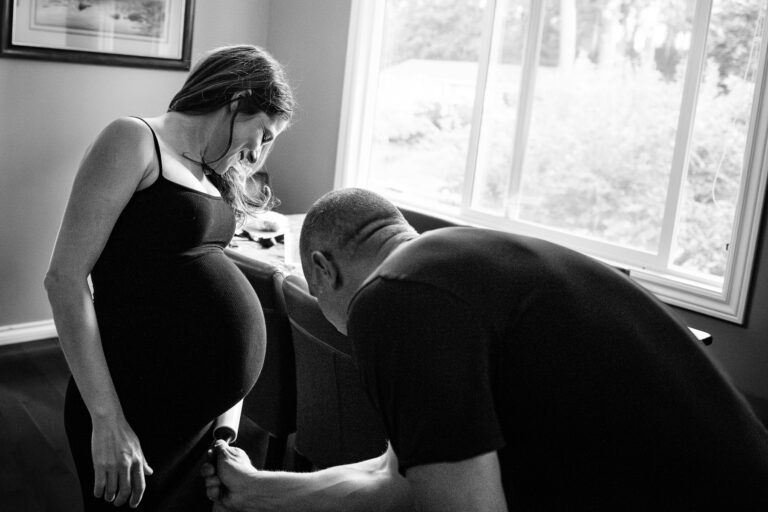 A father-to-be brushes off dog hair off mom-to-be's baby bump in their kitchen.