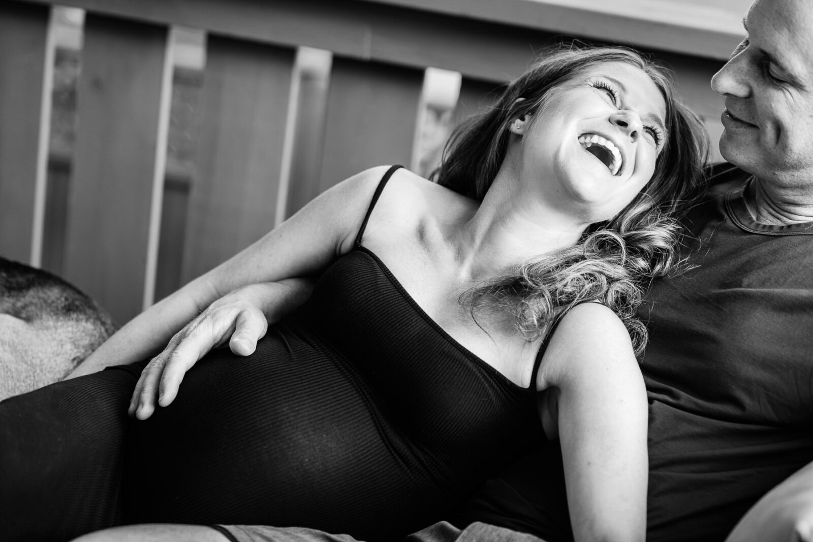 A mother to be looks at her partner and laughs while having a candid and natural maternity portrait session in their home in Victoria BC