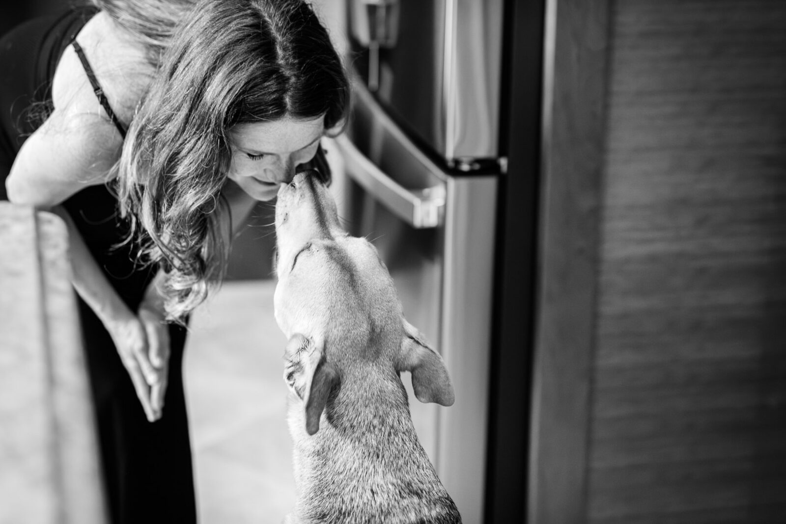 A candid photo of a dog kissing his mom's nose.