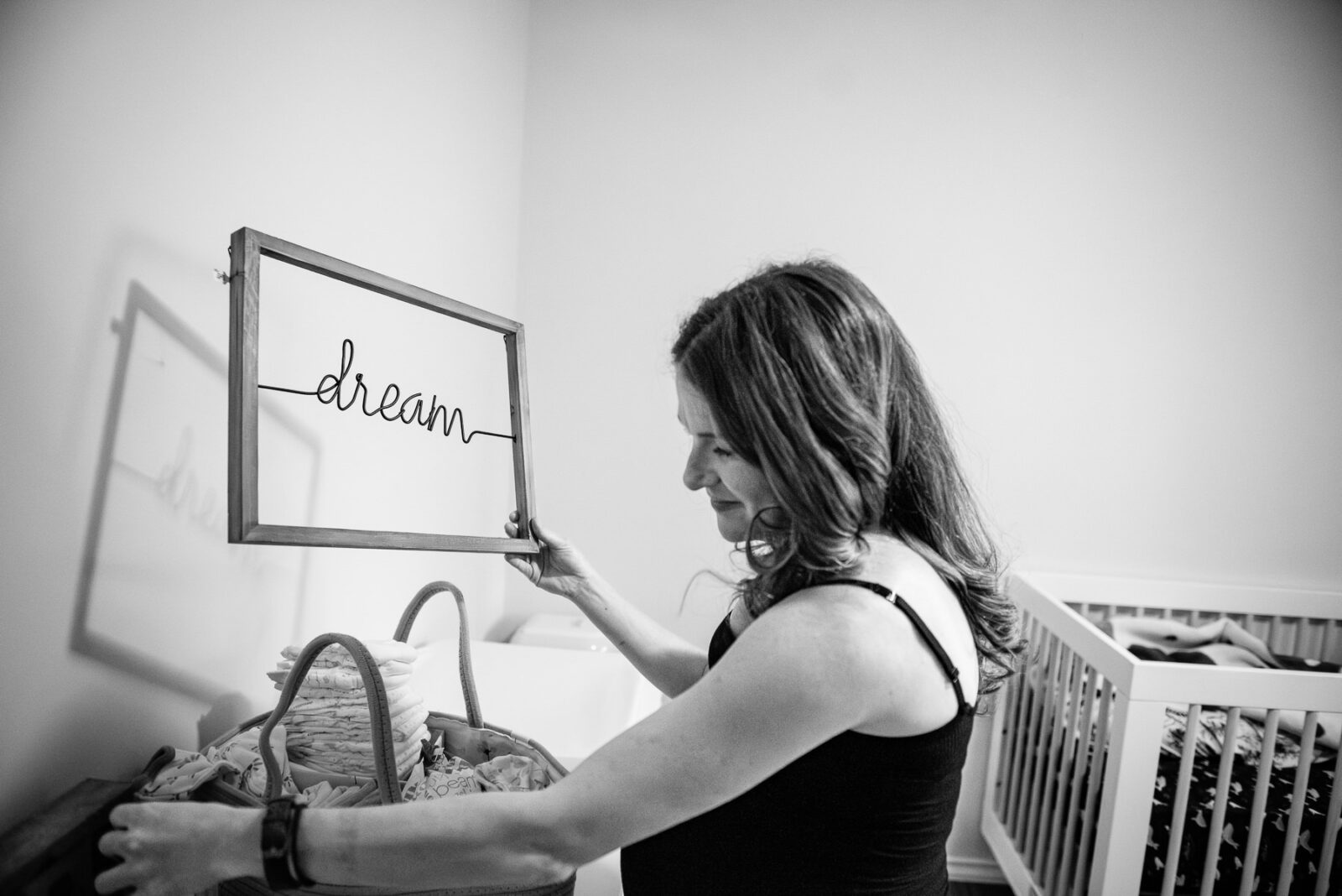 A mom-to-be holds up a dream art sign she will put on her nursery wall during a tour of their house.