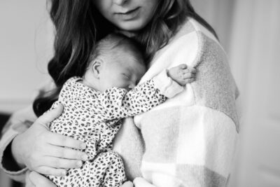A baby grips her mother's sweater. This is a candid, photojournalism portrait in Black and white taken in the nursery.