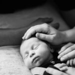 A baby being tenderly touched by her mother. This is a portrait taken in black and white on a bed in the family's home in Sooke.