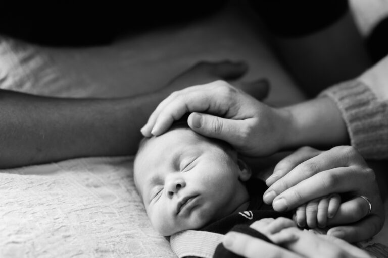 A baby being tenderly touched by her mother. This is a portrait taken in black and white on a bed in the family's home in Sooke.