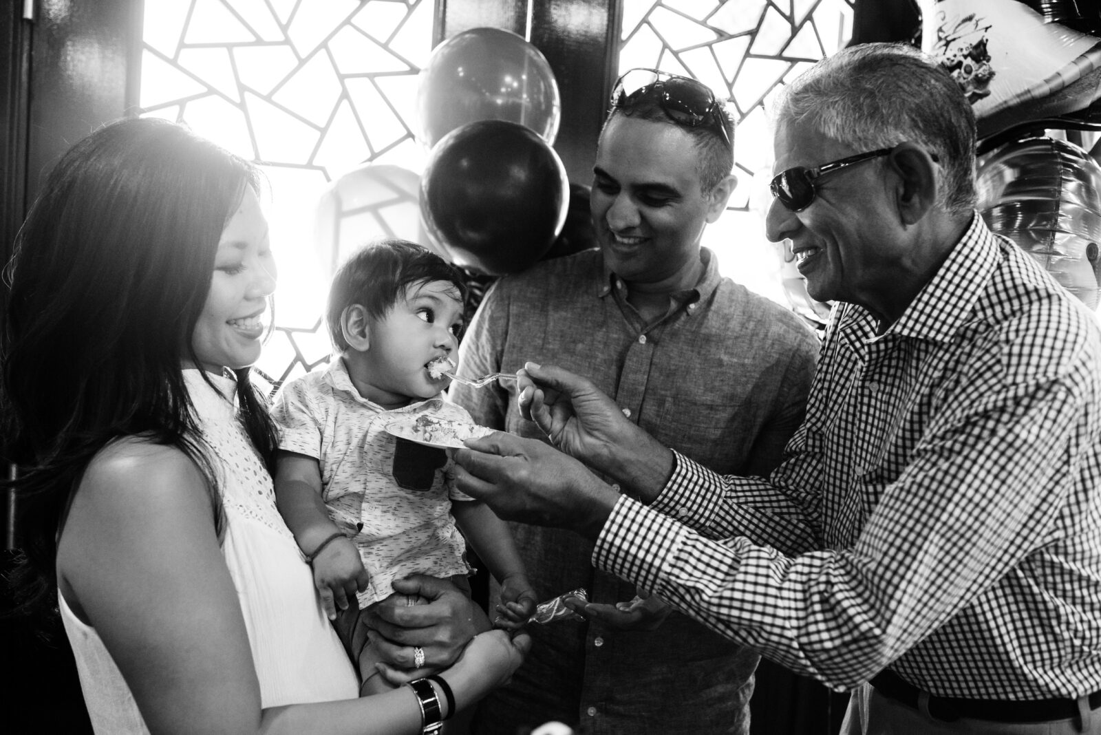 A birthday boy gets fed his first birthday party cake at Dr. Sun Yat-Sen Classical Chinese Garden in Vancouver BC. This is a candid photo in black and white.