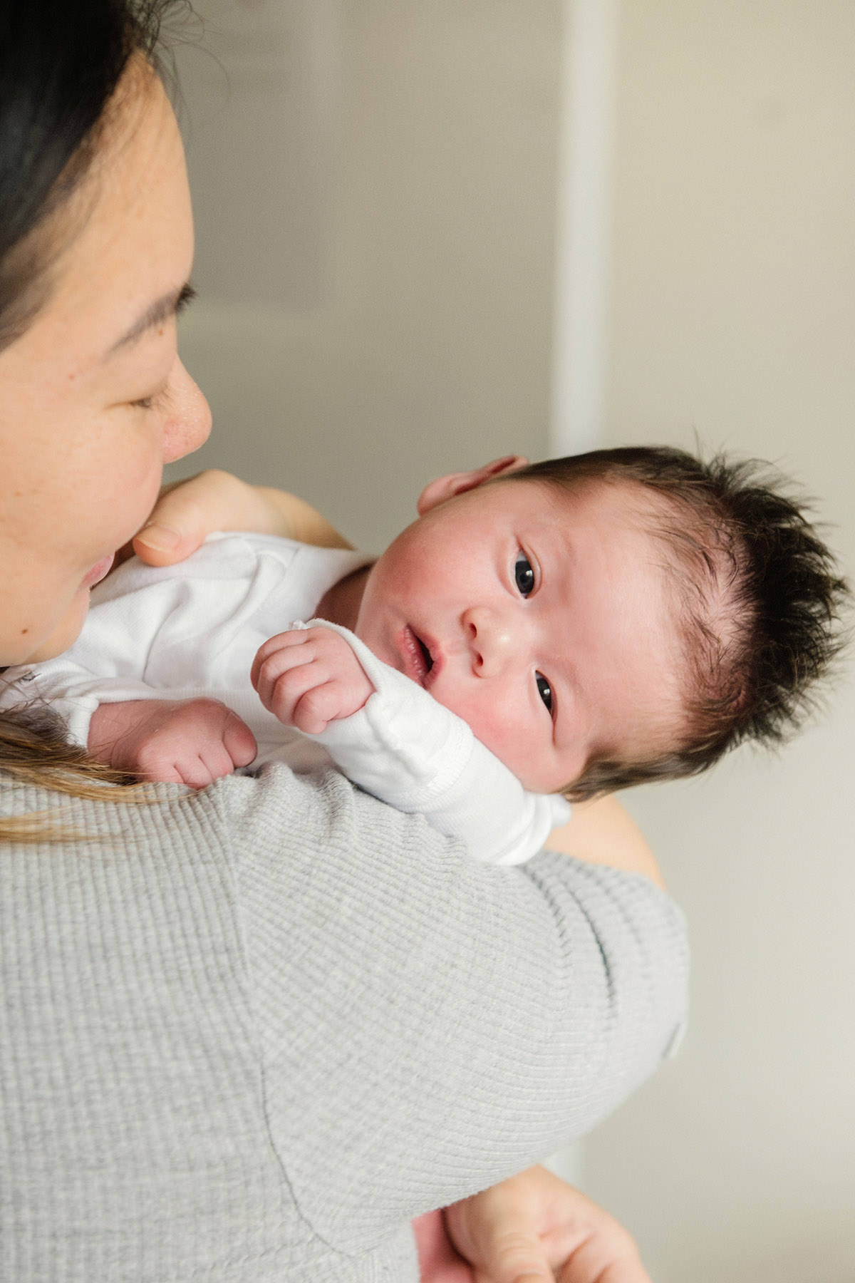 A newborn baby looks at the camera as her mother cradles her in the nursery of their home in Victoria BC on Vancouver Island.