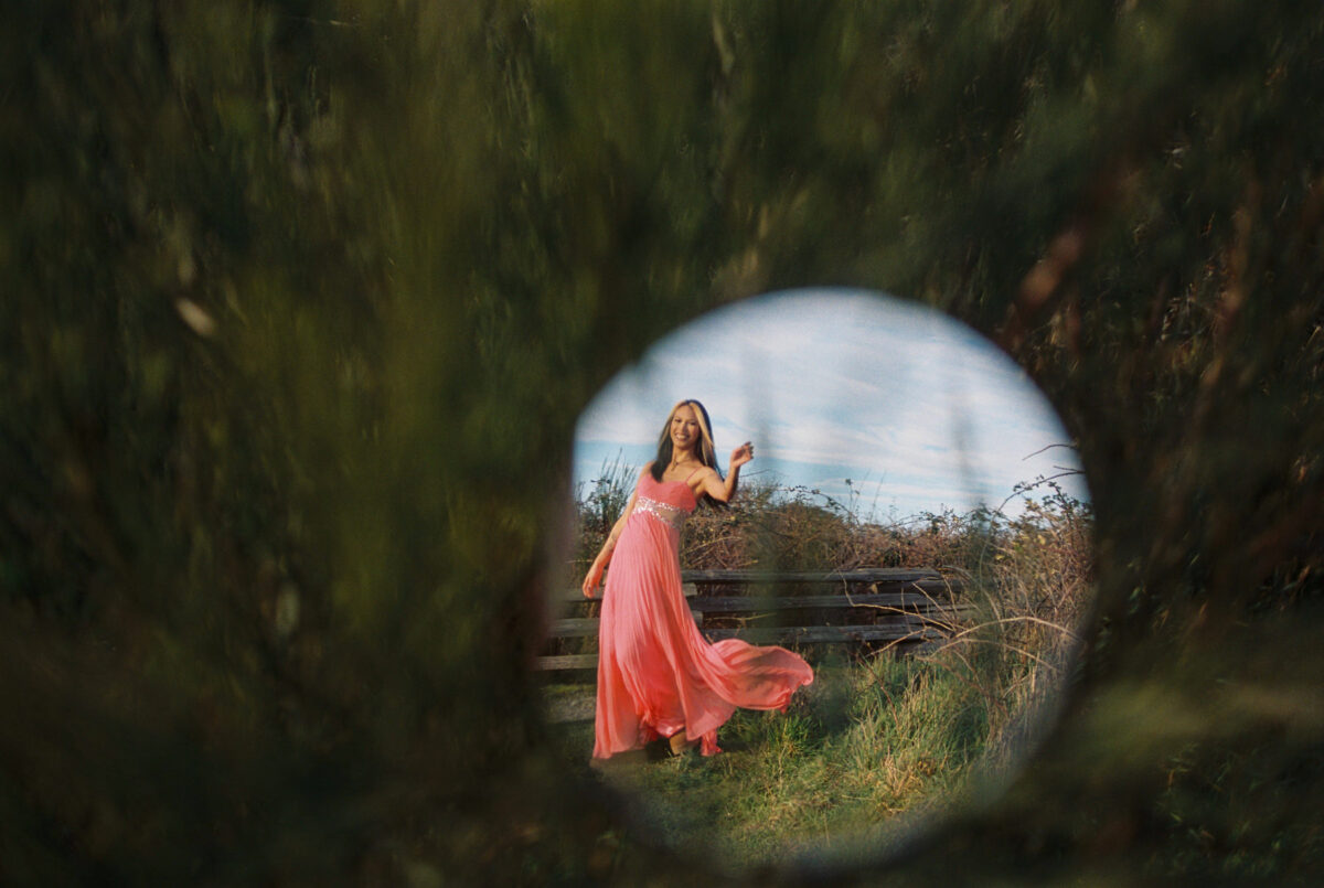 A creative picture of a fashion model in a pink dress twirling with her dress reflected in an acrylic mirror. This is a film photo taken at Macaulay Point Park. 