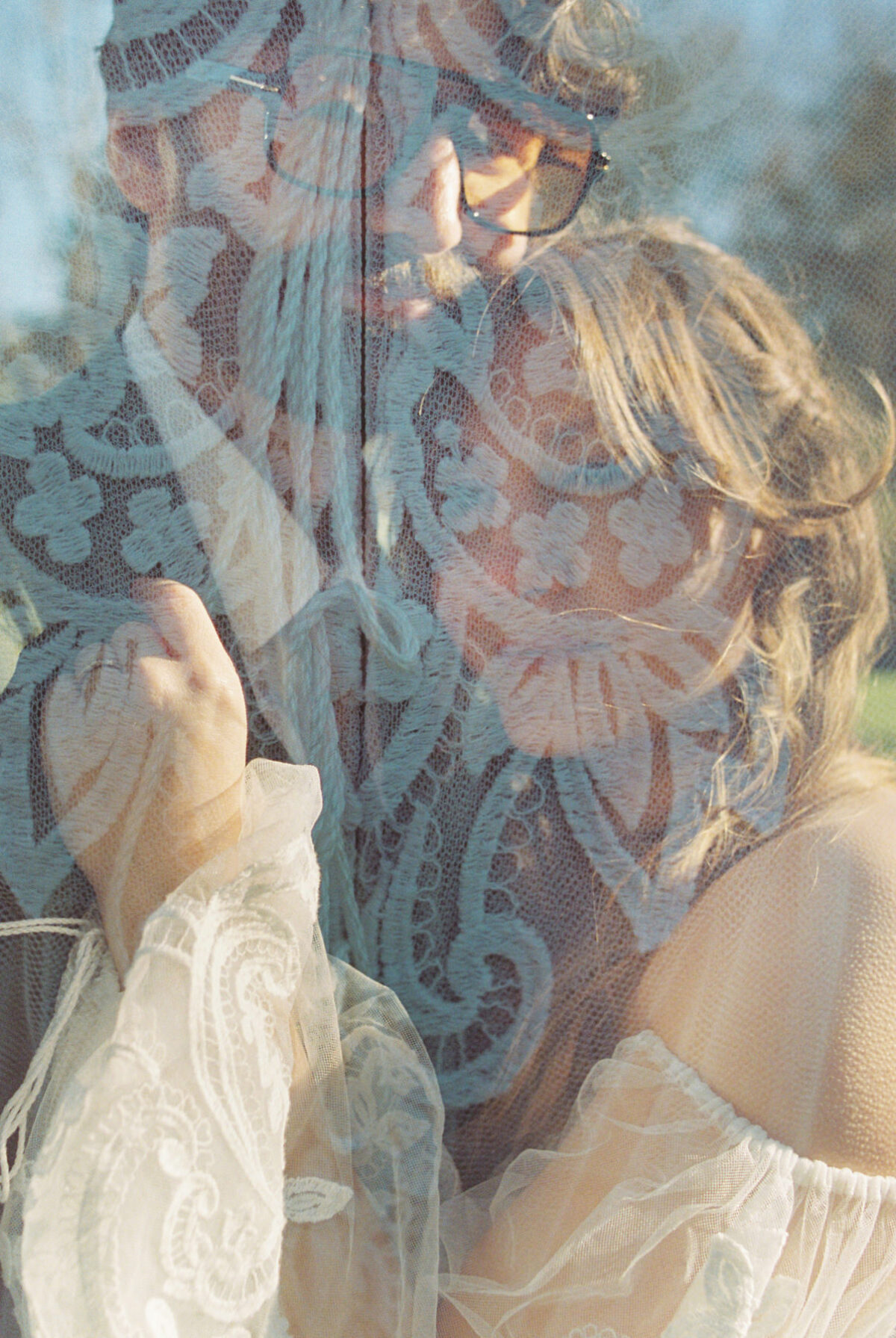 A creative artistic wedding photo of a double exposure on film showing a bride and groom cuddling into each other and the lace of the persephone gown overlaid on top of them. 