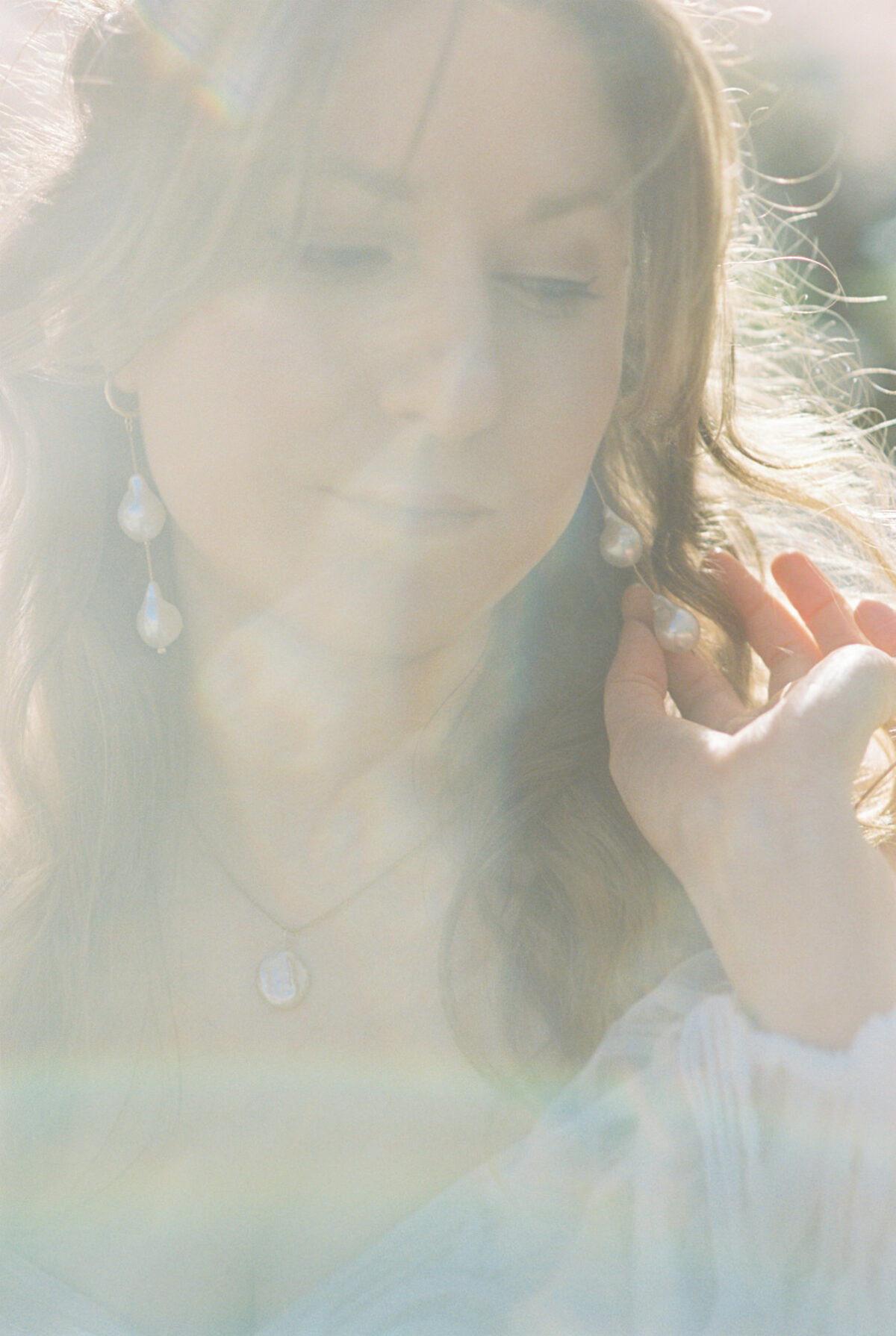 A soft bridal portrait on film where the bride is touching her pearl earrings during a film wedding photography session at UVic in Victoria BC