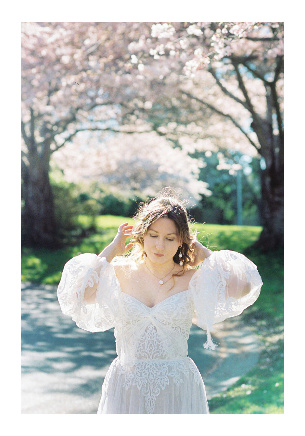 A bride plays with her hair with cherry blossoms in the background during an editorial wedding photo session at Uvic in spring when there were lots of cherry blossoms. This was photographed on analog film. 