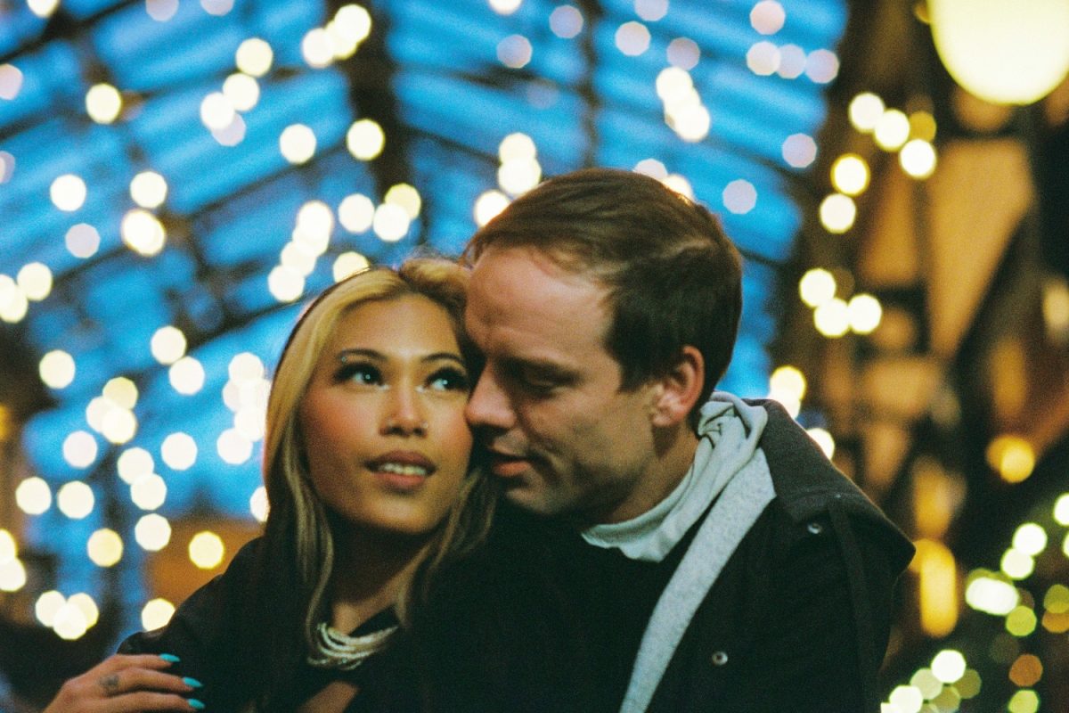 A couple surrounded by background bokeh lights at night are cuddling in an alley way in Victoria BC