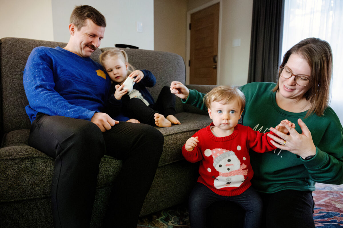 A family of four has a candid mini session in their home playing with their kids while wearing funny