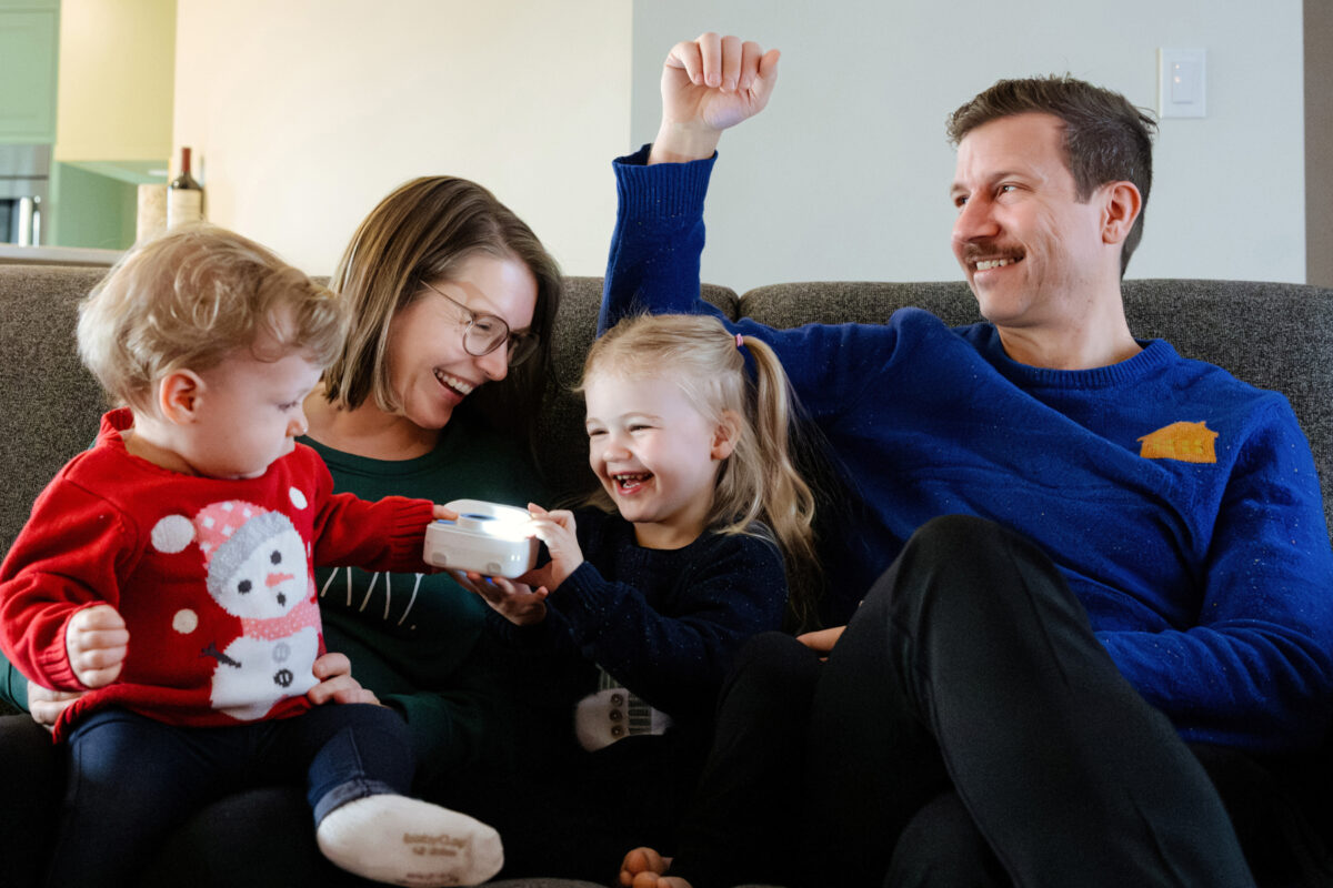 A fun at-home Christmas mini-session in Victoria BC. A family of four with two toddlers sits on the couch together and laughs