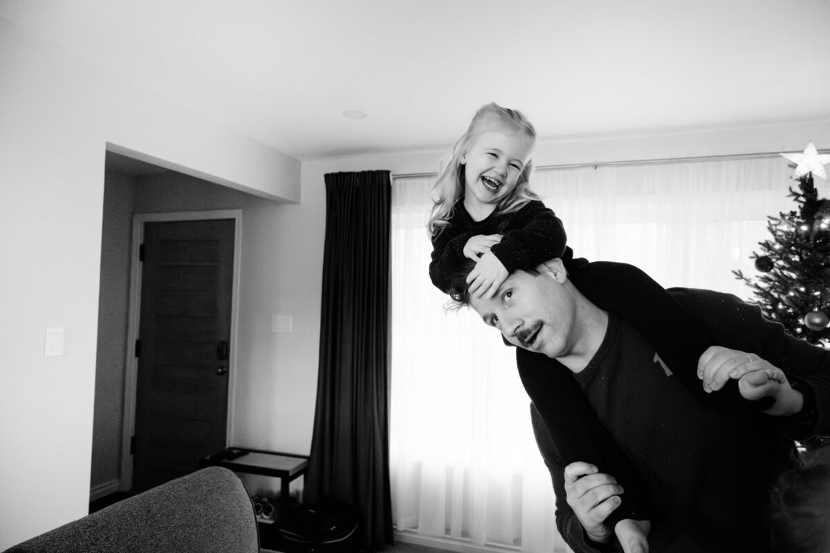A funny photo of a child on her father's shoulder during a Christmas mini session in Victoria BC in a family home. 