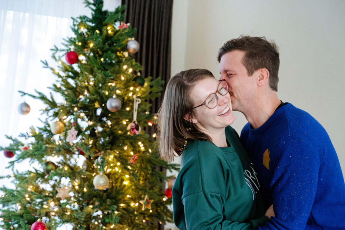 Parents kiss in front of the Christmas tree during their mini session in Victoria BC