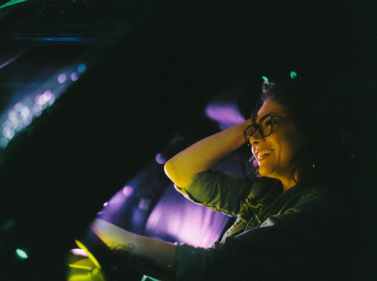 Cinematic night portrait of a woman in her car with street lights and video lights illuminating her. She is looking into the car window. This was taken on Cinestill 800T 120 film at box speed with a Pentax 645nii camera.