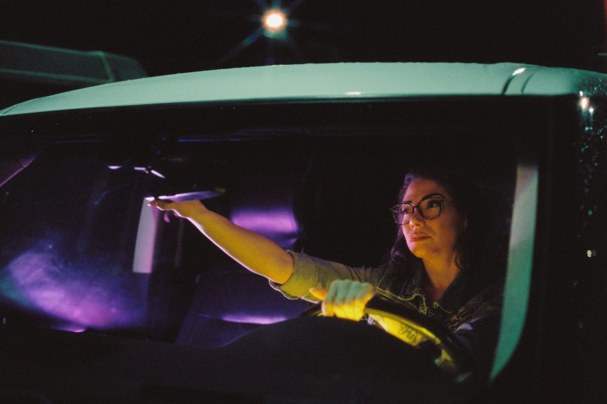 Cinematic night portrait of a woman in her car with street lights and video lights illuminating her. She is looking into the car window. This was taken on Cinestill 800T 120 film at box speed with a Pentax 645nii camera.