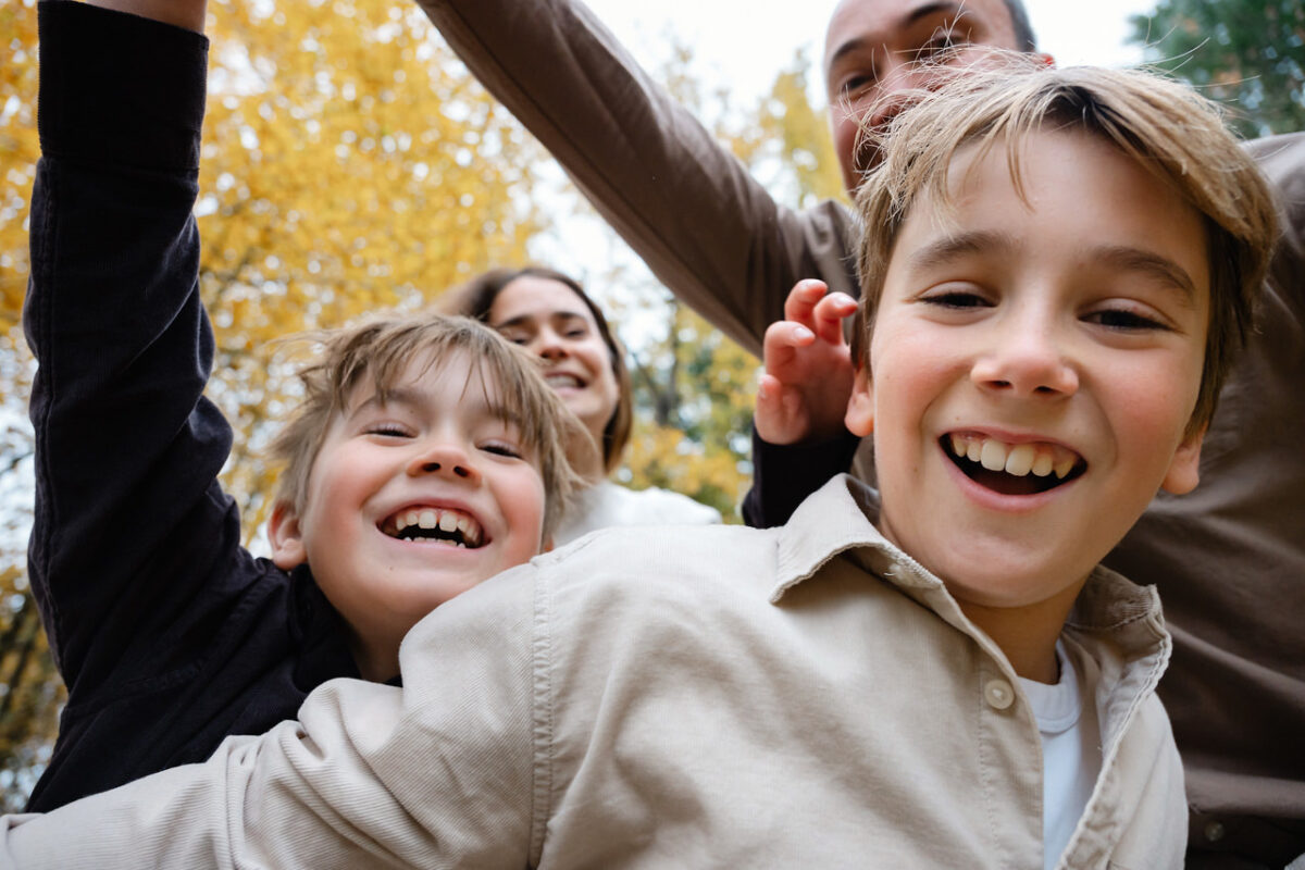 Portrait of a family laughing and being silly in front of the camera at Elk Lake in Victoria BC during the fall when there are tons of coloured leaves on the ground.