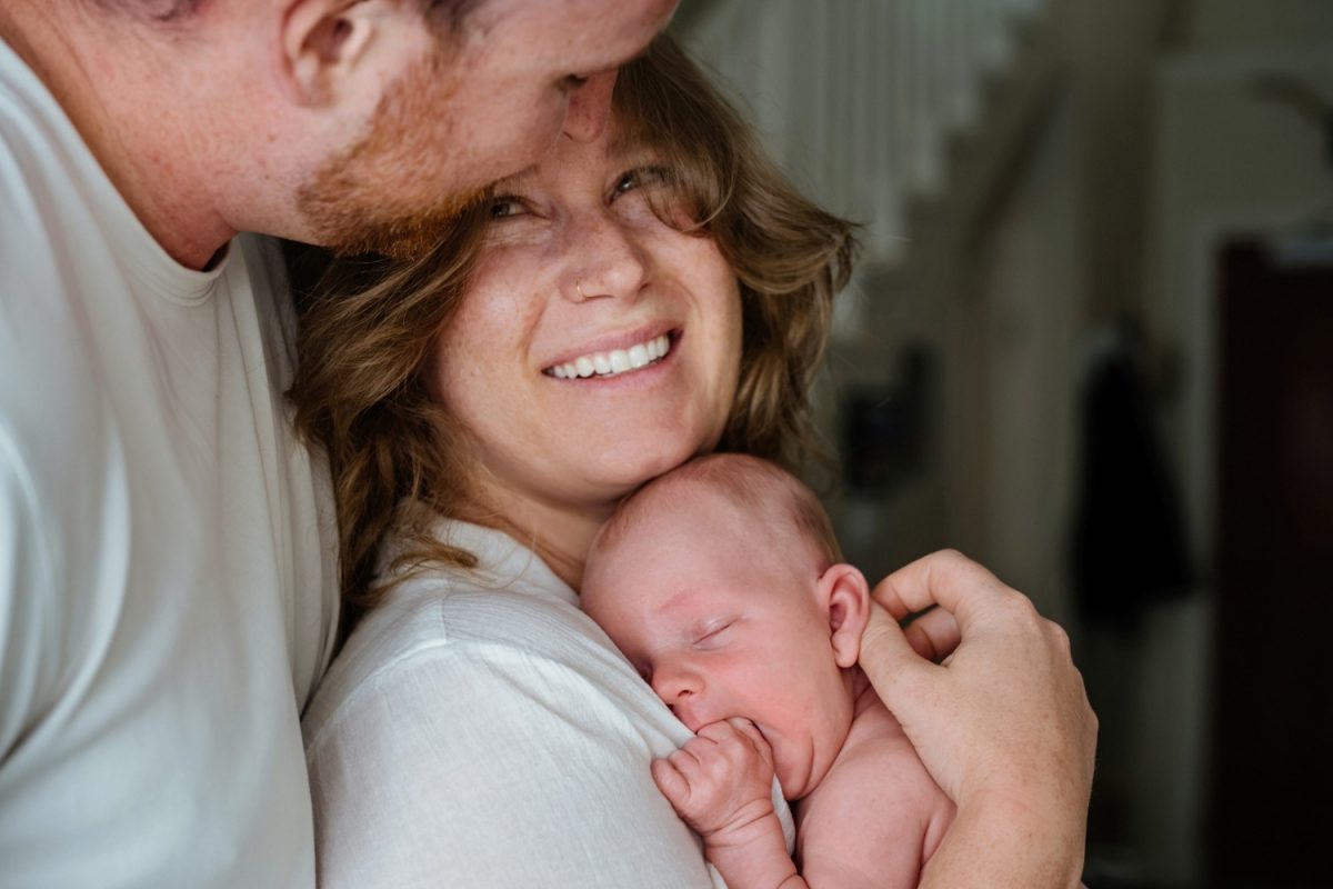 A candid documentary photojournalism image of parents holding their baby during an at-home newborn photo session in Langford BC