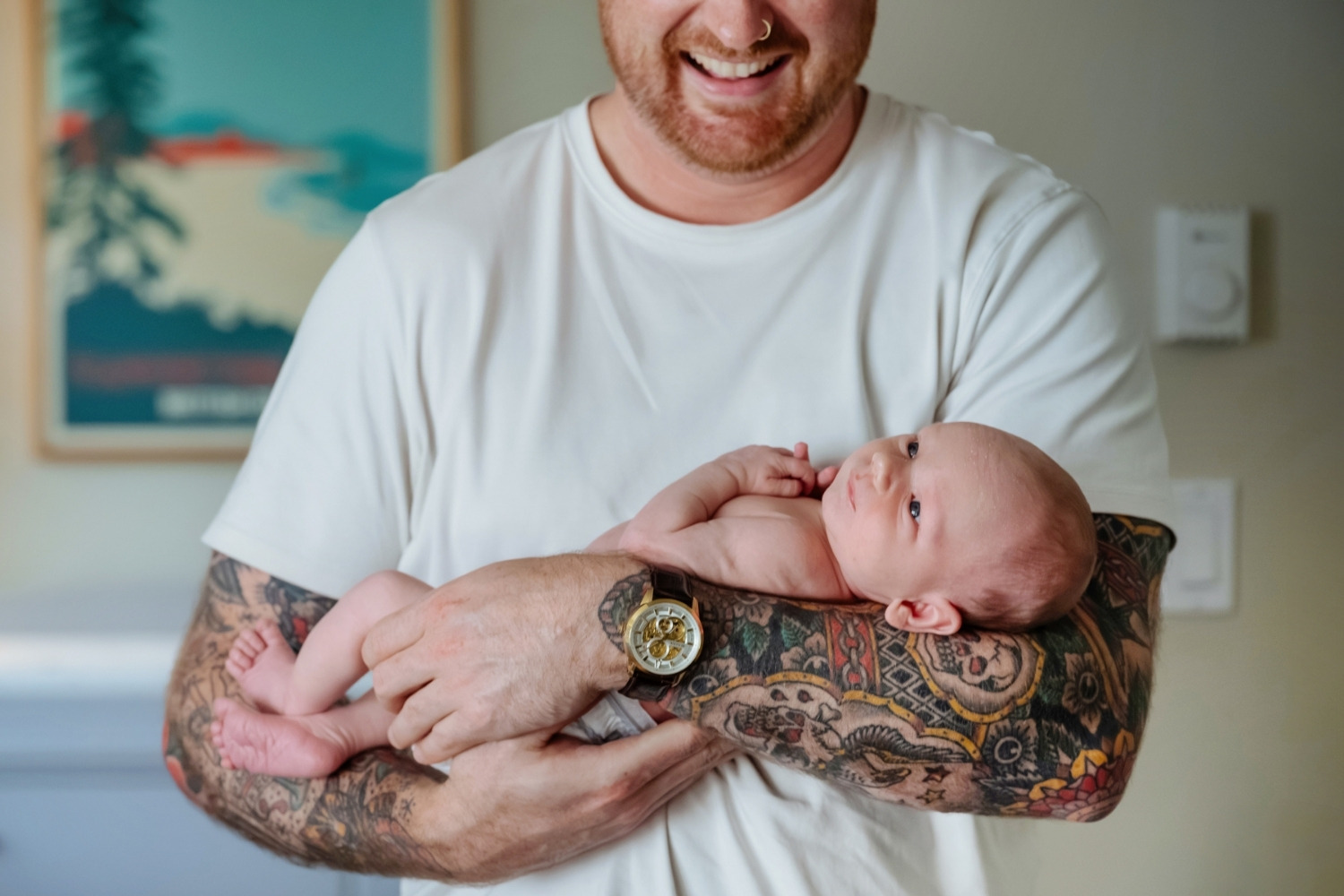A tattooed father holds his newborn baby during an at-home newborn session in Langford BC