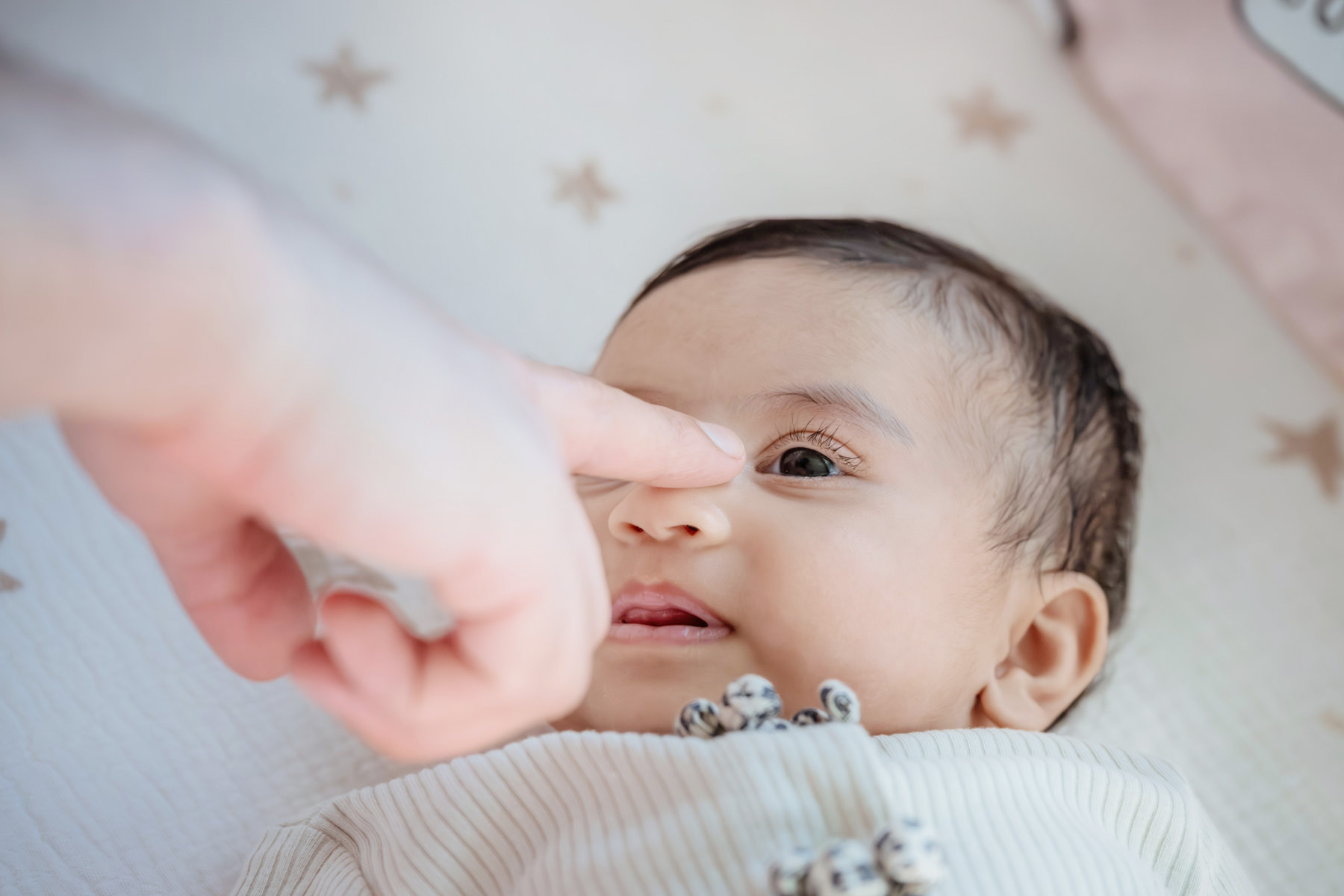A father boops his baby's nose while she lays in her crib during a candid baby portrait session in the family home.